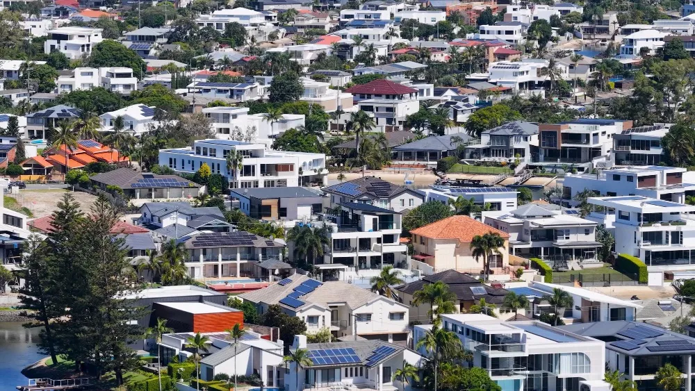 Aerial view of a dense waterfront suburb of white and terracotta-roofed houses with solar panels, palm trees and a canal