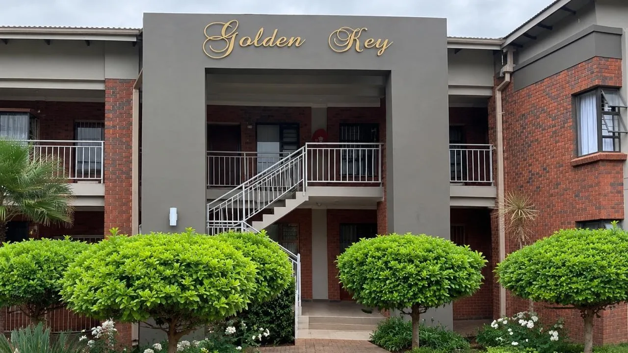 Golden Key apartment block in Die Bult, Potchefstroom: two-storey face-brick building with a grey entrance arch, an open staircase and round clipped trees along a paved path