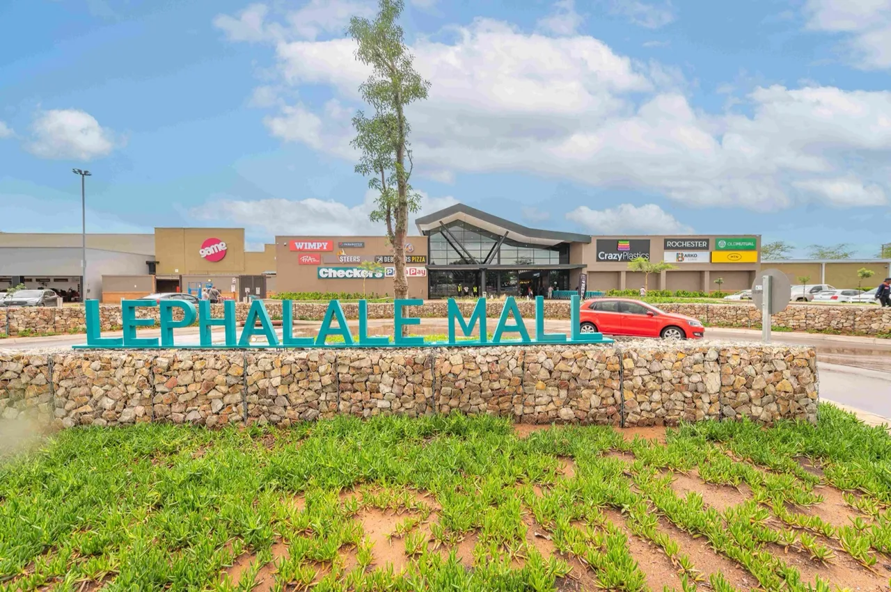 Lephalale Mall: large teal letters spelling Lephalale Mall on a stone gabion wall in front of the single-storey centre, with Game, Wimpy, Checkers, Crazy Plastics and Rochester signage under a blue sky