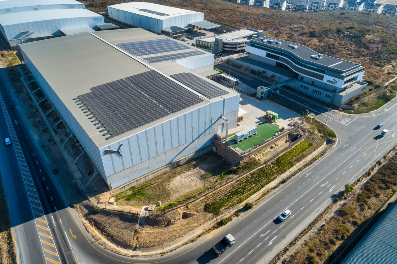 Aerial view of an Equites logistics park at Atlantic Hills, Cape Town, with a large Puma-branded warehouse with rooftop solar panels beside the Puma office building and a motorway